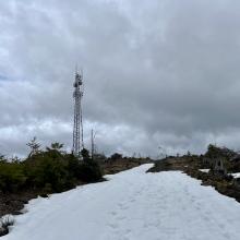 Snowy trail showing peak with gate at the top and radio tower on peak