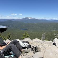 Man with umbrella relaxing on summit with mountain view in background